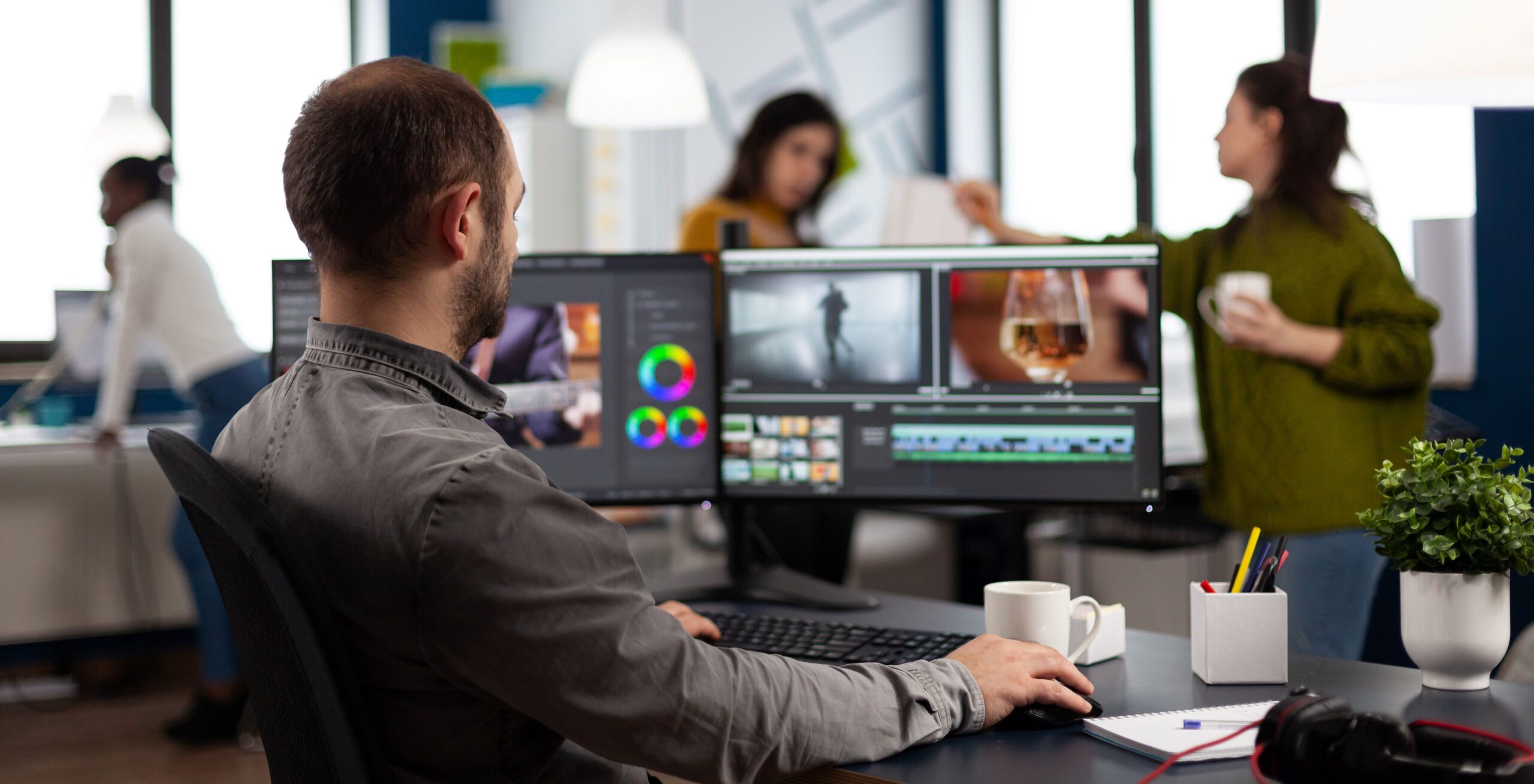Videoeditor schneidet Filmmaterial bei der Montage von Filmen am Computer mit zwei Monitoren im Büro einer Multimedia-Kreativagentur.